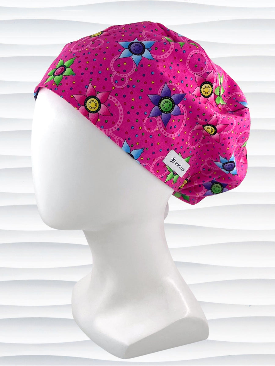 Euro Pixie style surgical scrub cap hat with bright purple, blue, and green flowers and pink circles on pink cotton fabric.