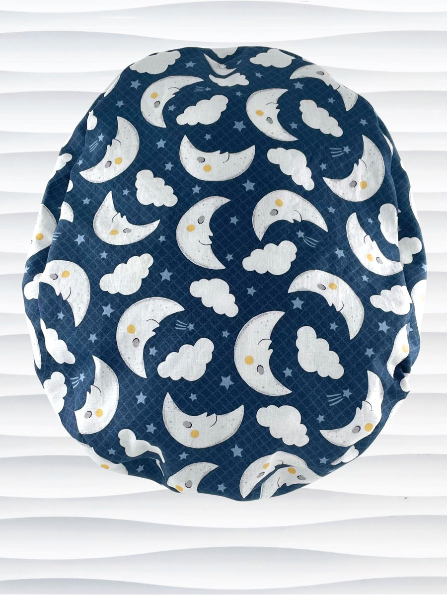 Pony freeform style surgical scrub cap hat with white moons and clouds and blue shooting stars on dark blue cotton fabric.