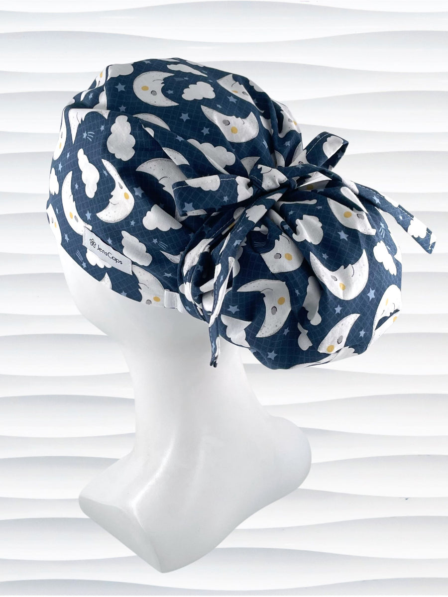 Pony freeform style surgical scrub cap hat with white moons and clouds and blue shooting stars on dark blue cotton fabric.