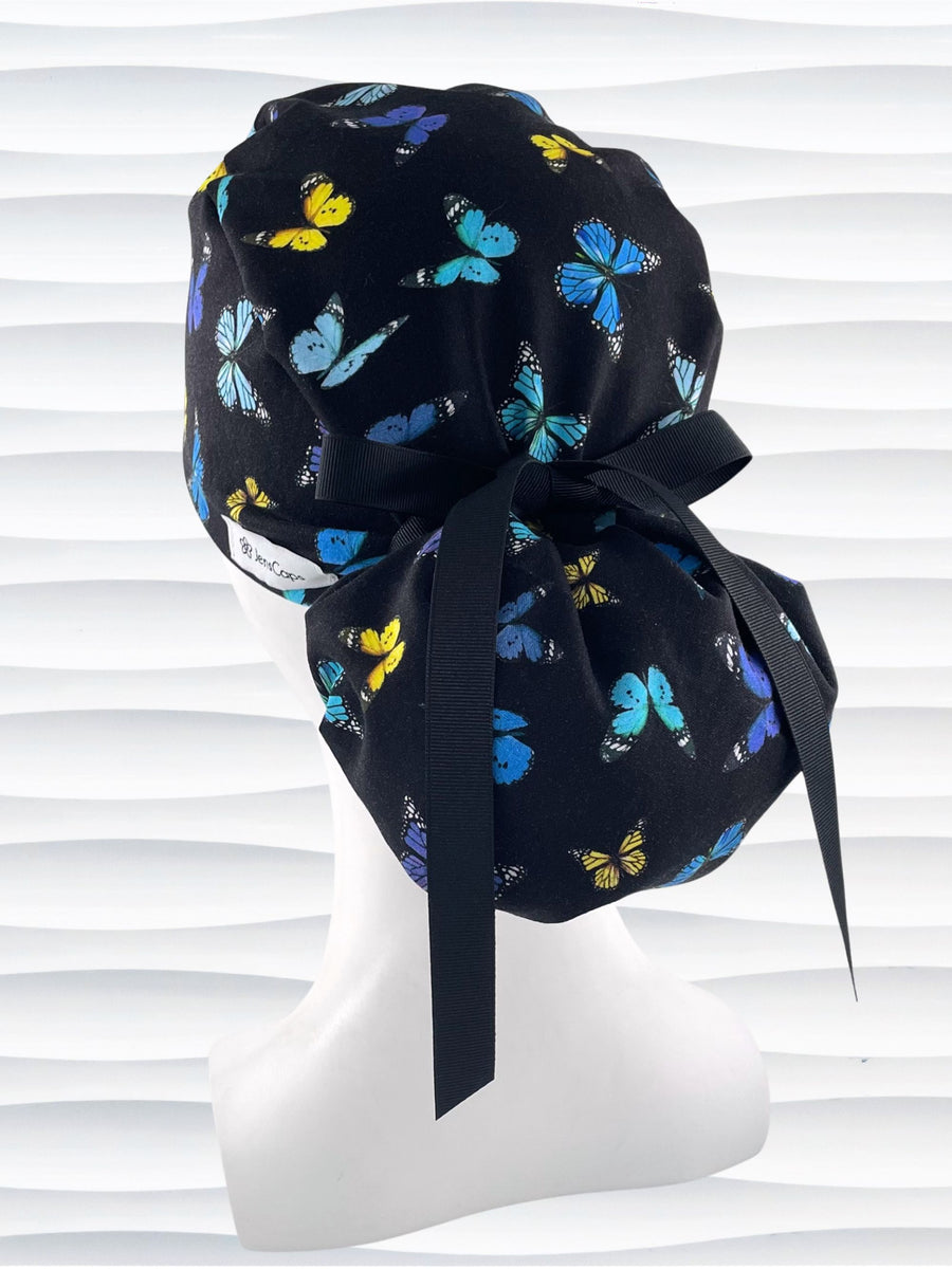 Ponytail style surgical scrub cap hat with blue, purple, and yellow butterflies all over black cotton fabric.