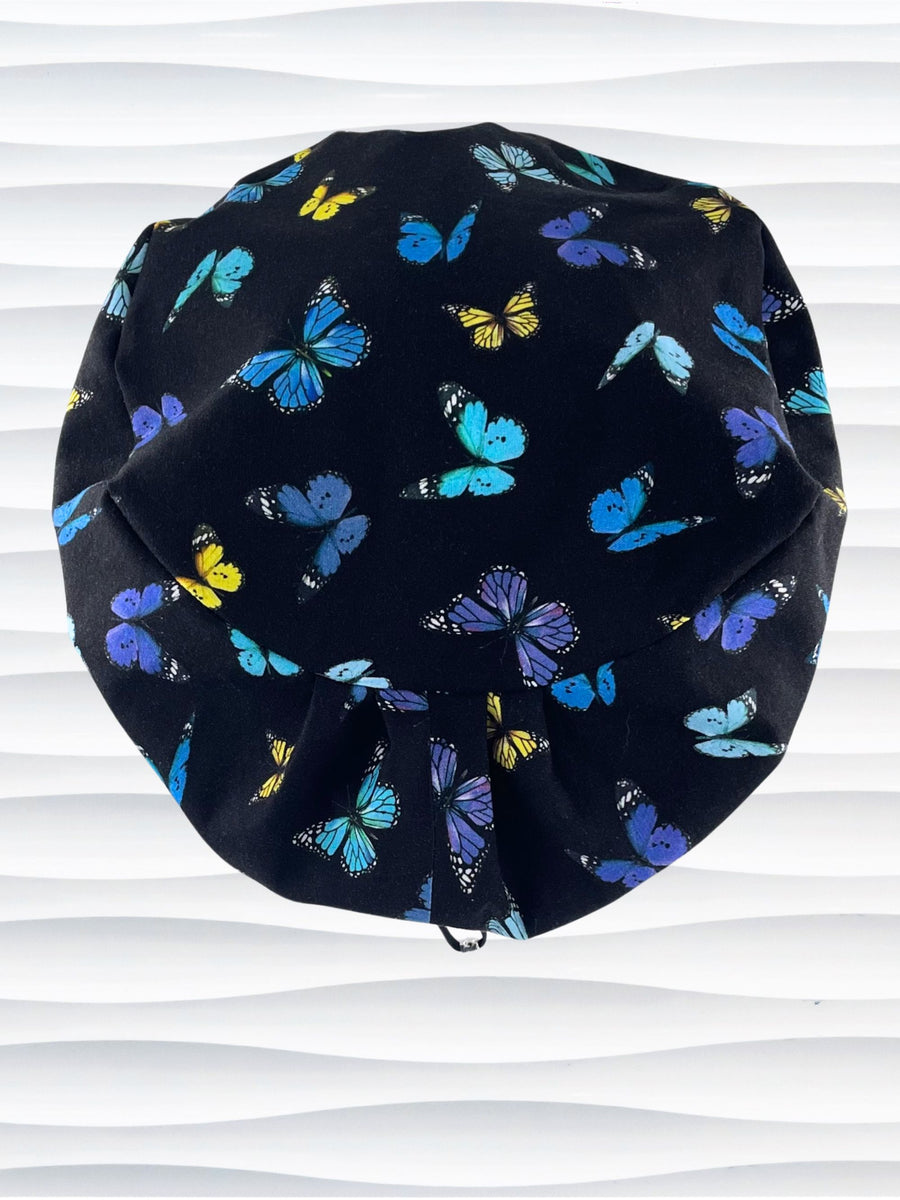 Euro Pixie style surgical scrub cap hat with blue, purple, and yellow butterflies all over black cotton fabric.