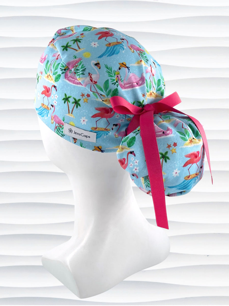 Ponytail surgical scrub cap hat with surfing flamingos, tropical drinks, leis, flowers, and sunglasses on blue cotton fabric.