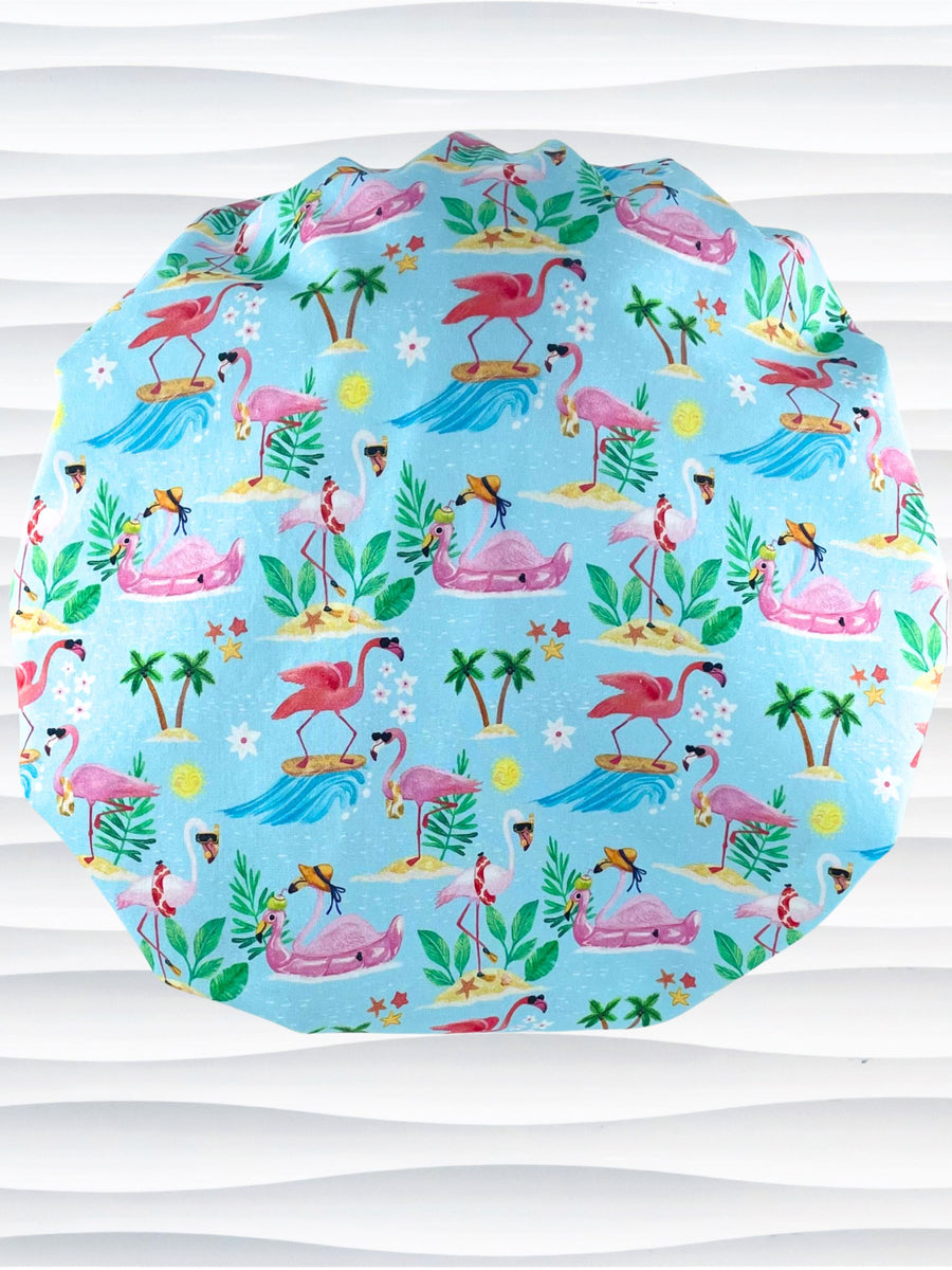 Bouffant style surgical scrub cap hat with cute flamingos, tropical flowers, island drinks, and surf waves on light blue cotton fabric.