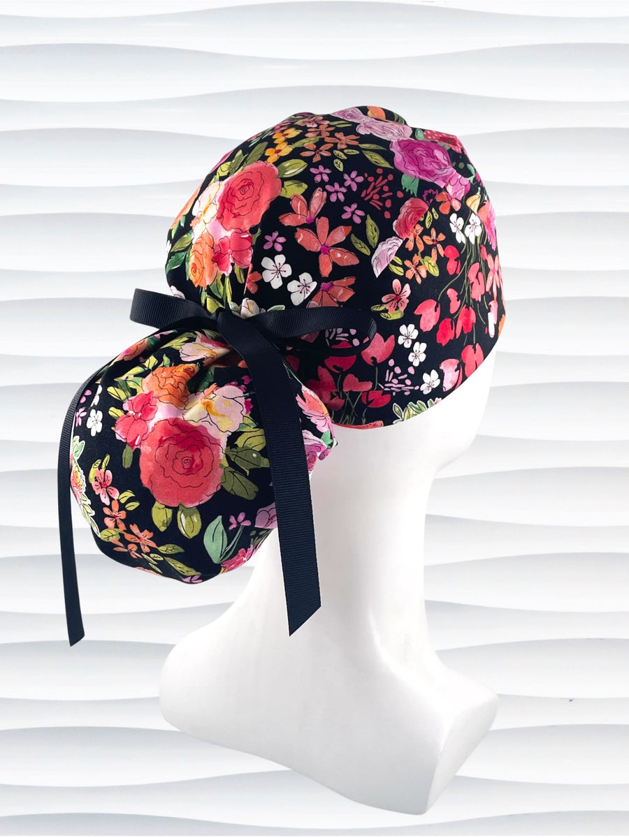 Ponytail style surgical scrub cap hat with pink, red, yellow, and orange flowers on black premium cotton fabric.