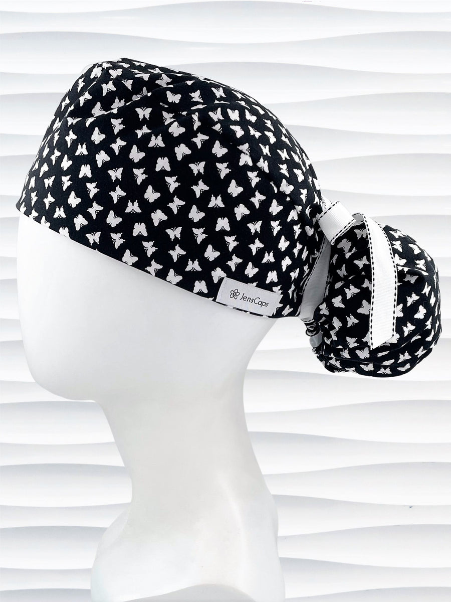 Ponytail style scrub cap hat with white butterflies on black cotton fabric.