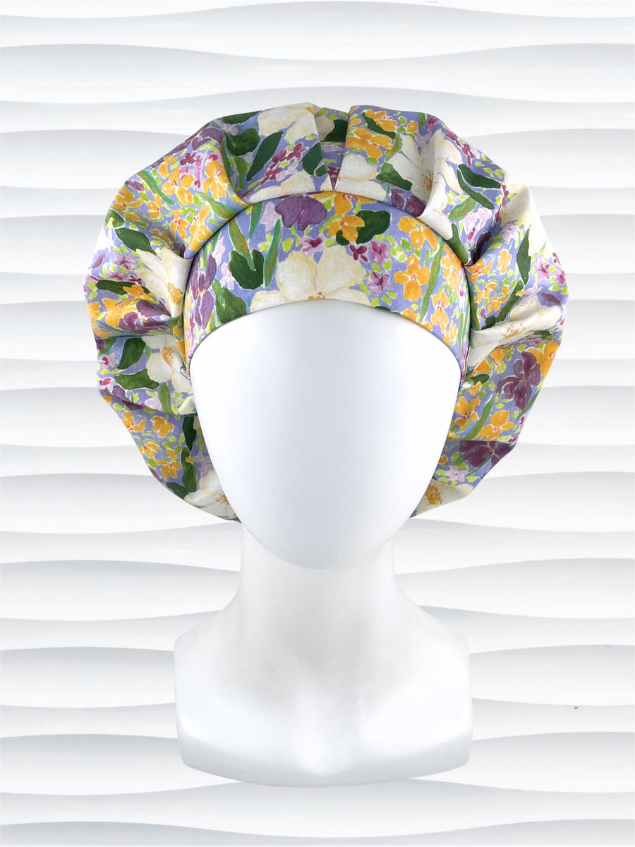 Bouffant style surgical scrub cap hat with Mardi Gras colors of yellows, greens, and purples on white cotton fabric.