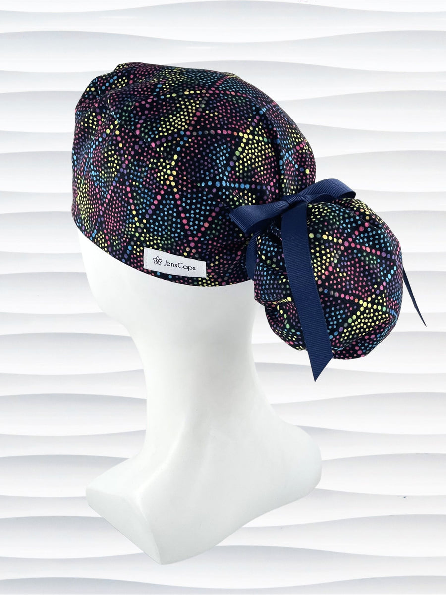 Ponytail style surgical scrub cap hat with bright colored dots and lines in diamond shapes on black cotton fabric.