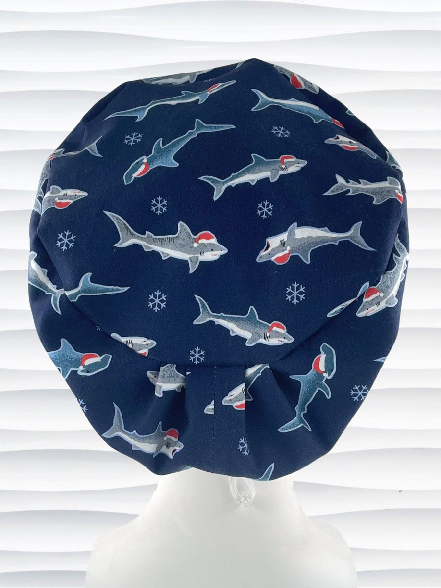 Pixie euro style surgical scrub cap hat with snowflakes and sharks wearing Santa hats on dark blue cotton fabric.