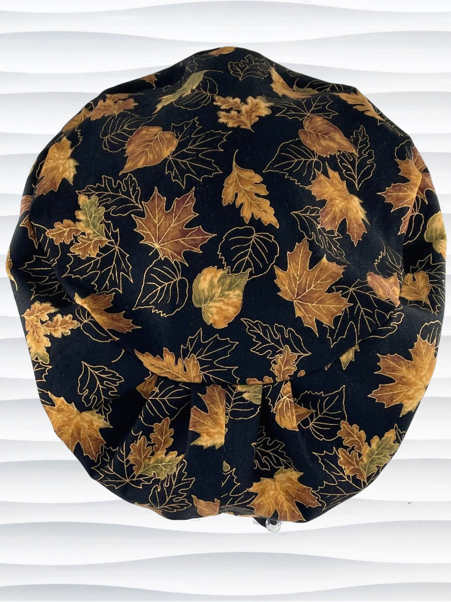 Pixie Euro style surgical scrub cap hat with leaves outlined with gold metallic accents on black cotton fabric.