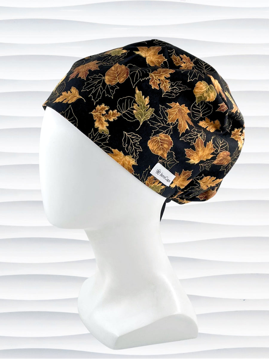 Pixie Euro style surgical scrub cap hat with  leaves outlined with gold metallic accents on black cotton fabric.