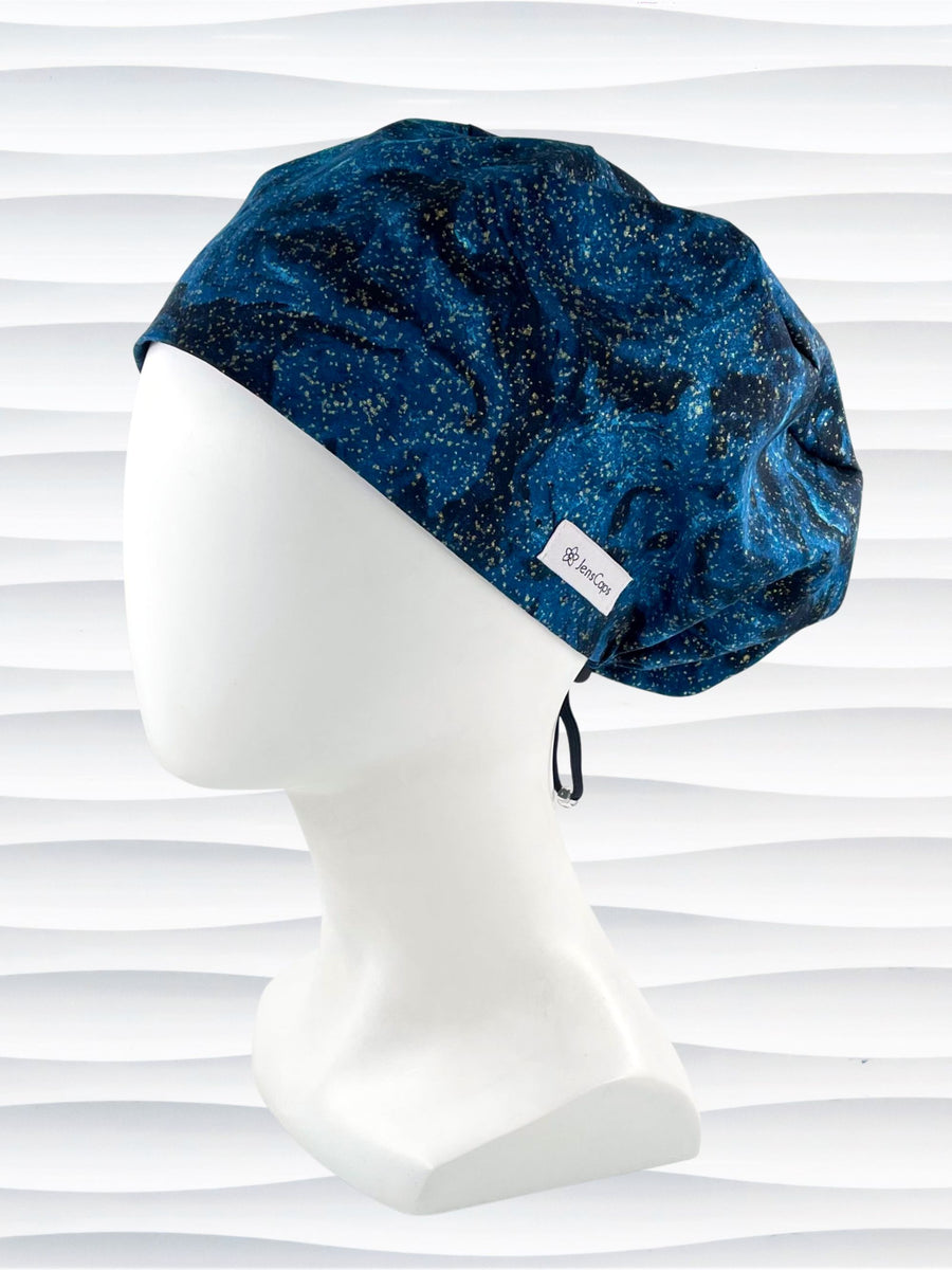 Pixie Euro style surgical scrub cap hat with an oil slick design with gold metallic accents on dark blue cotton fabric.