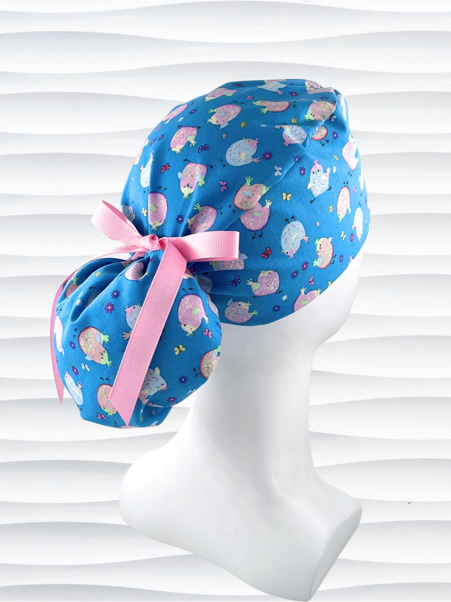 Ponytail style surgical scrub cap hat with cute pink and blue Easter baby chickens with butterflies and flowers on blue cotton fabric.
