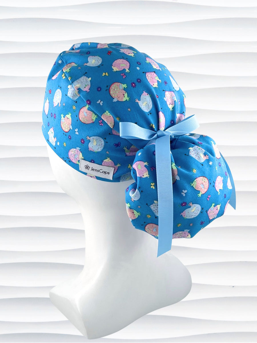 Ponytail style surgical scrub cap hat with cute pink and blue Easter baby chickens with butterflies and flowers on blue cotton fabric.