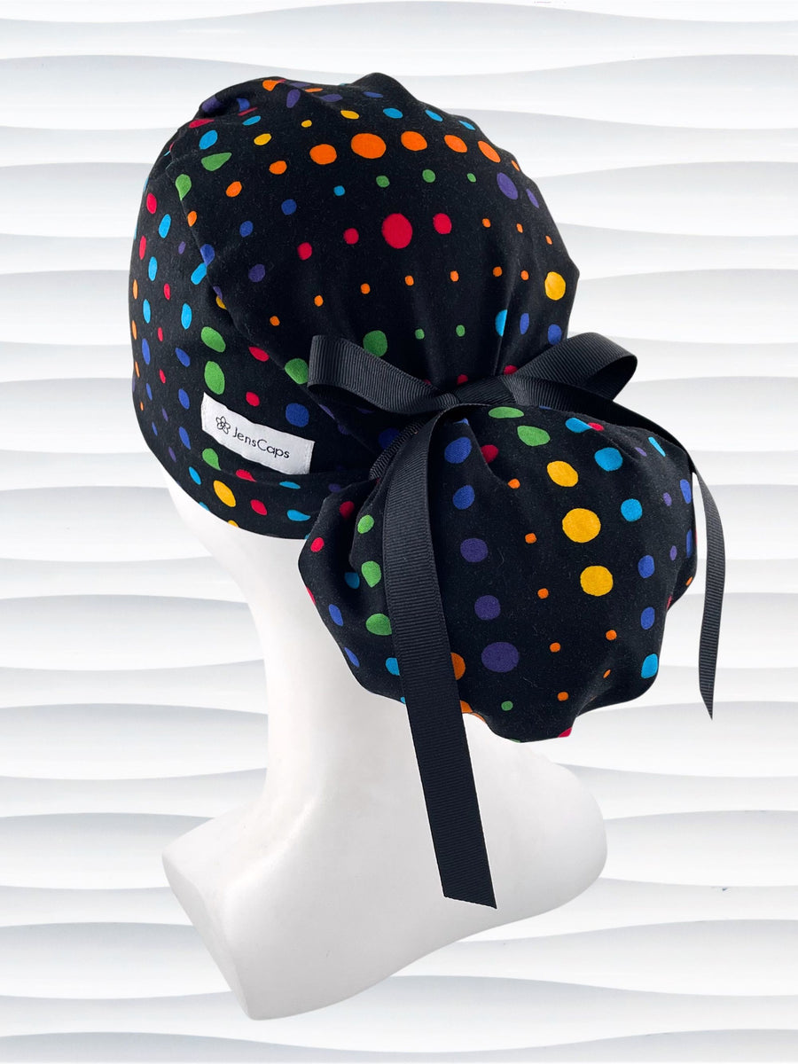 Ponytail style surgical scrub cap hat with circles in primary colors in a linear design on black cotton fabric.