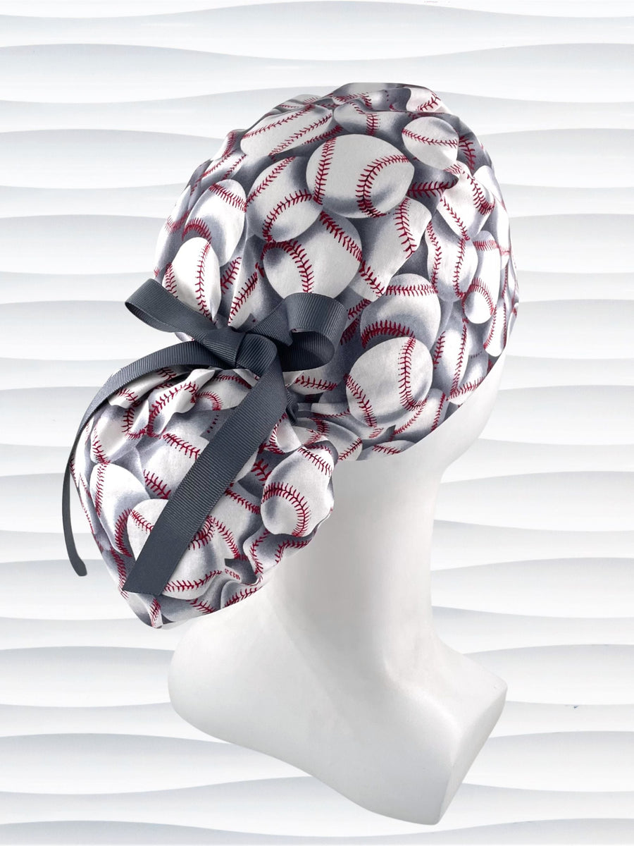 Ponytail style surgical scrub cap hat with white baseballs with red stitching on light gray cotton fabric and finished with grosgrain ribbon.