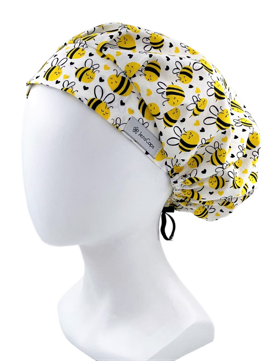 Bouffant style surgical cap hat for women.  This cotton fabric has an allover print of yellow and black bumble bees with yellow and black hearts tossed around on a white background.
