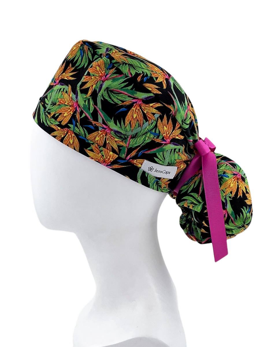 Ponytail style surgical scrub cap hat. This cotton fabric has an allover print of bird of paradise flowers and stems on a black background and finished with a black or pink grosgrain ribbon