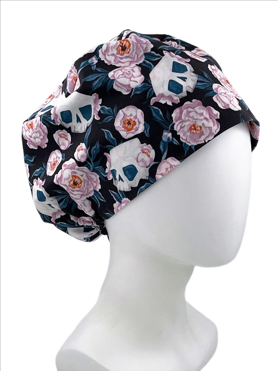 Pixie Euro style surgical scrub cap hat.  This cotton fabric has an allover print of flowers and skulls in pink and blue on a dark background.