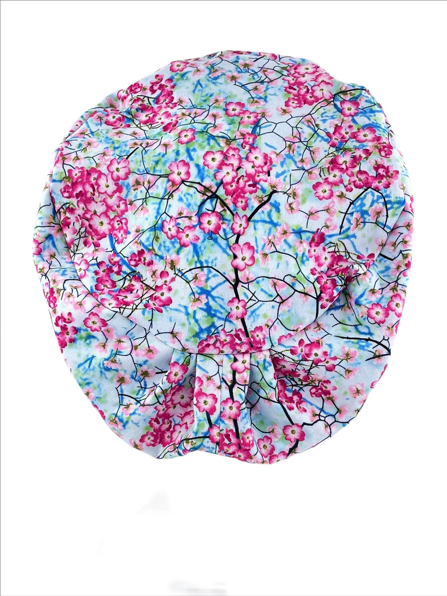 Bouffant style surgical scrub cap hat. This premium cotton fabric has cherry flower blossoms and branches on a blue sky background