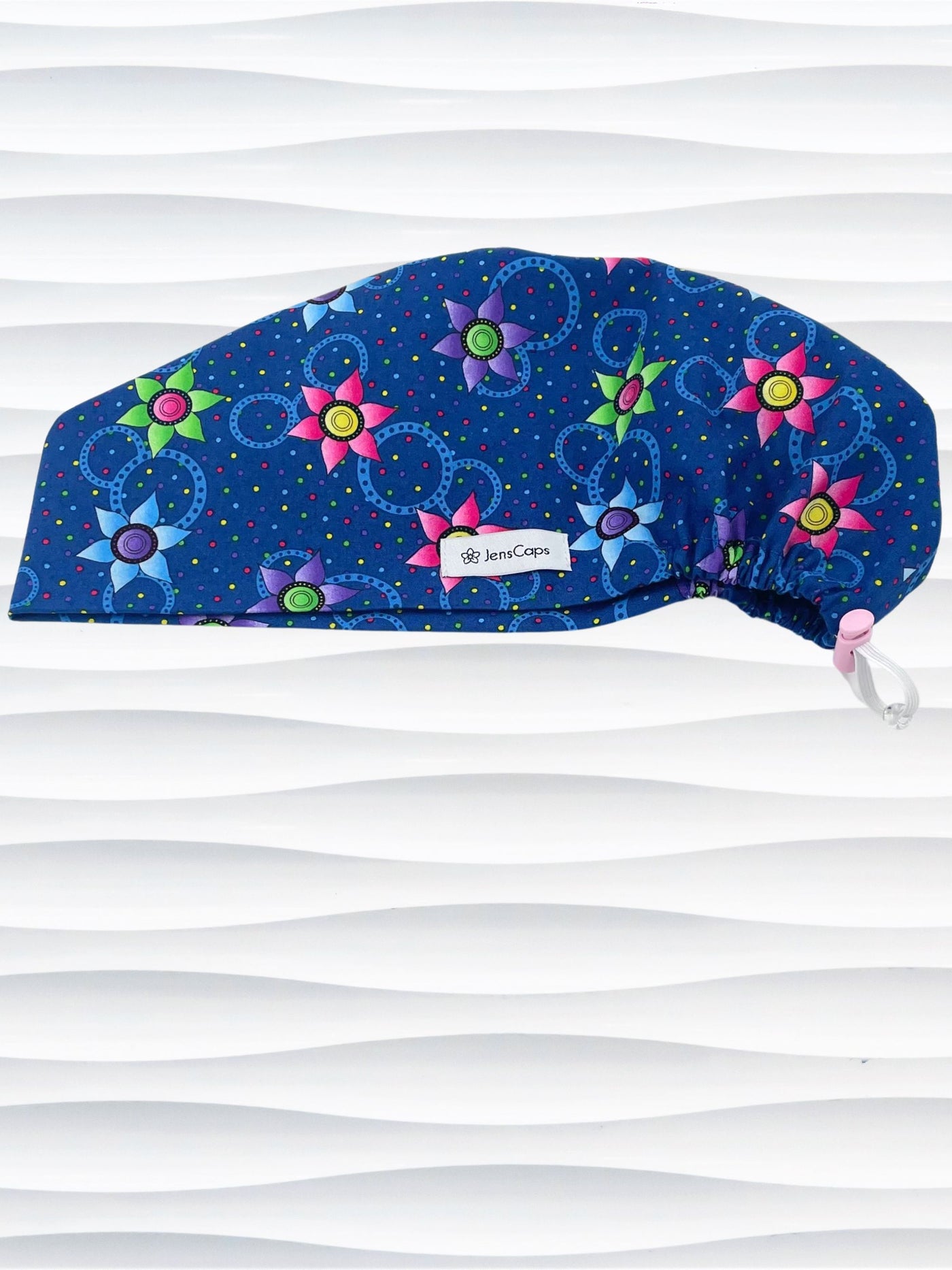 Euro Pixie style surgical scrub cap hat with bright pink, blue, and green flowers and blue circles on dark blue cotton fabric.