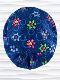 Euro Pixie style surgical scrub cap hat with bright pink, blue, and green flowers and blue circles on dark blue cotton fabric.