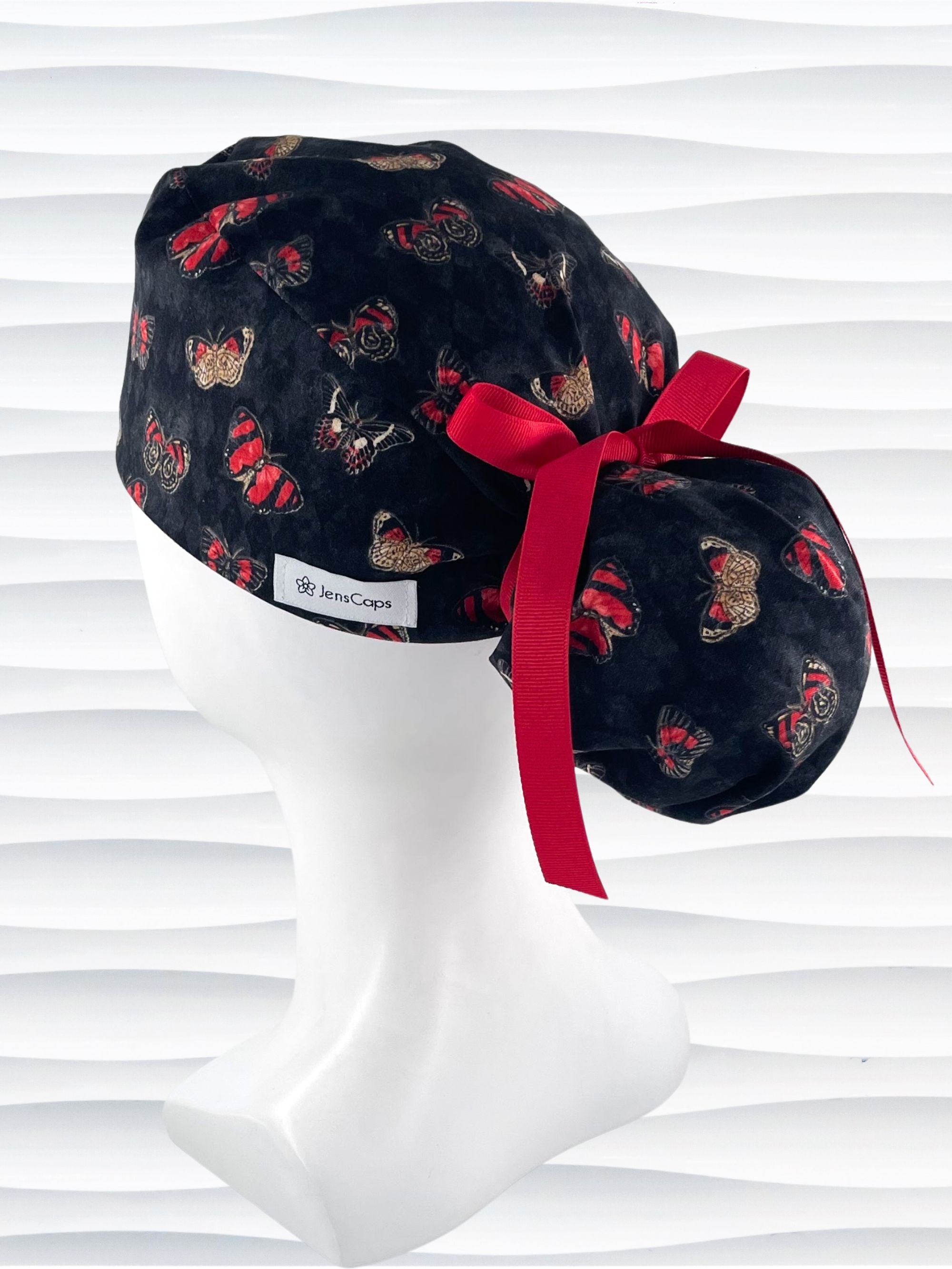 Ponytail style surgical scrub cap hat with red and black butterflies on a black harquin patterned background cotton fabric.