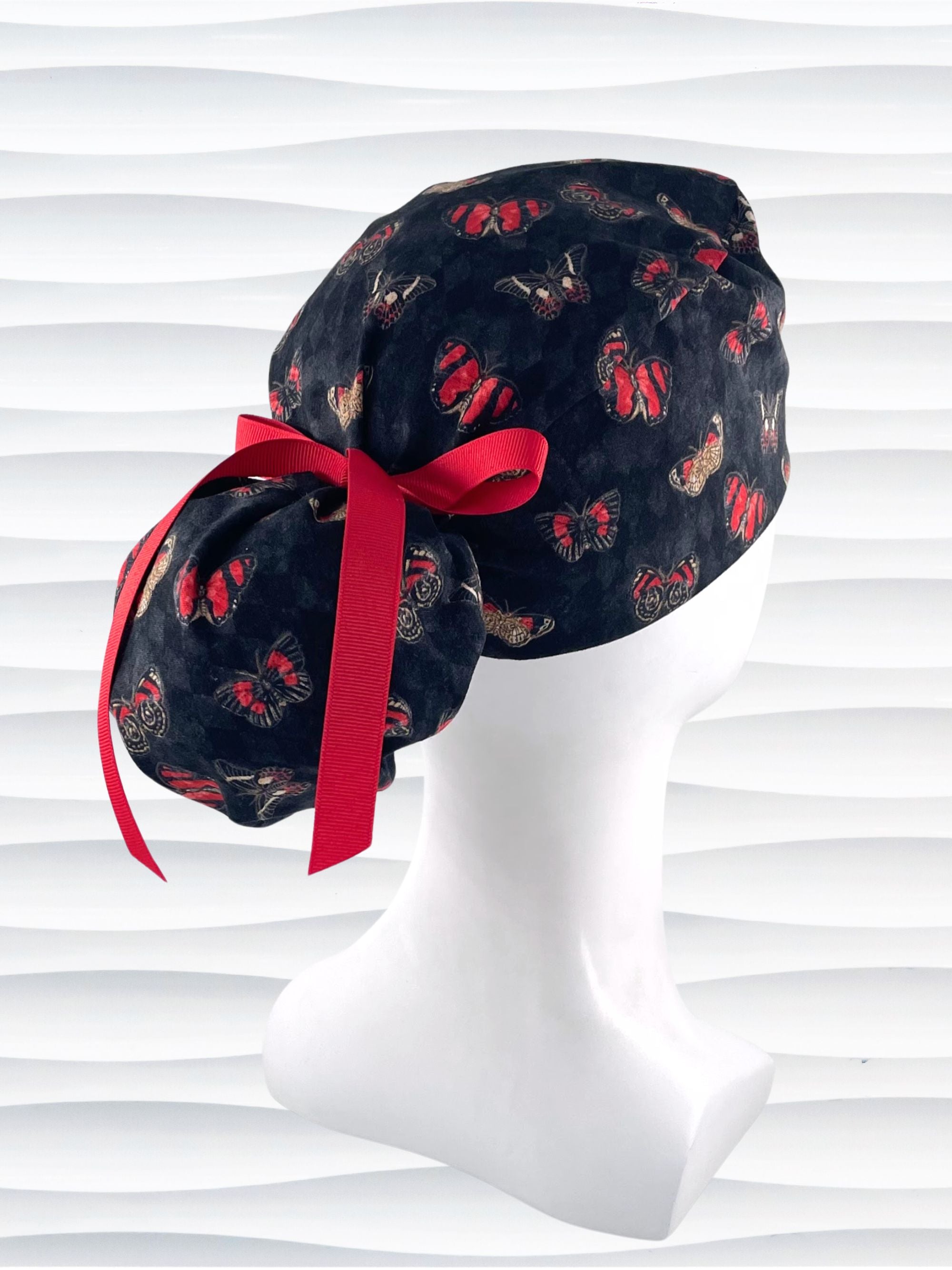 Ponytail style surgical scrub cap hat with red and black butterflies on a black harquin patterned background cotton fabric.