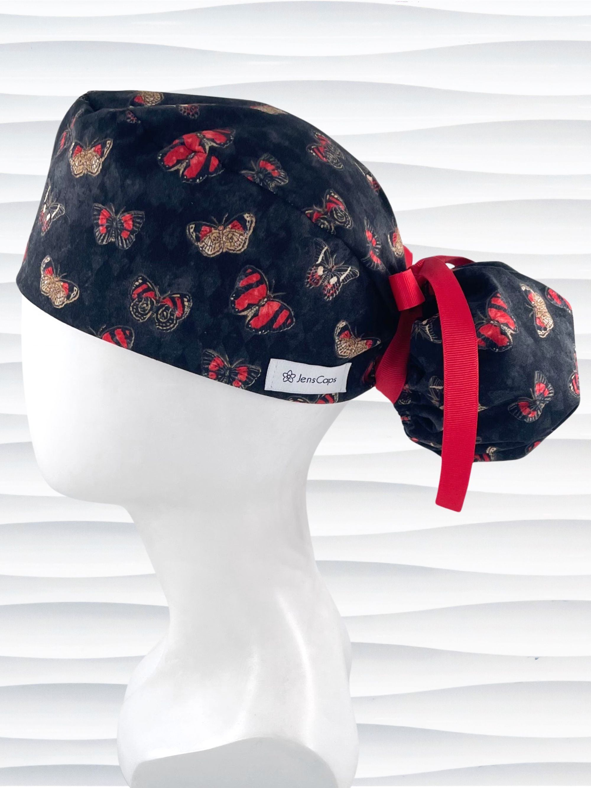 Ponytail style surgical scrub cap hat with red and black butterflies on a black harquin patterned background cotton fabric.