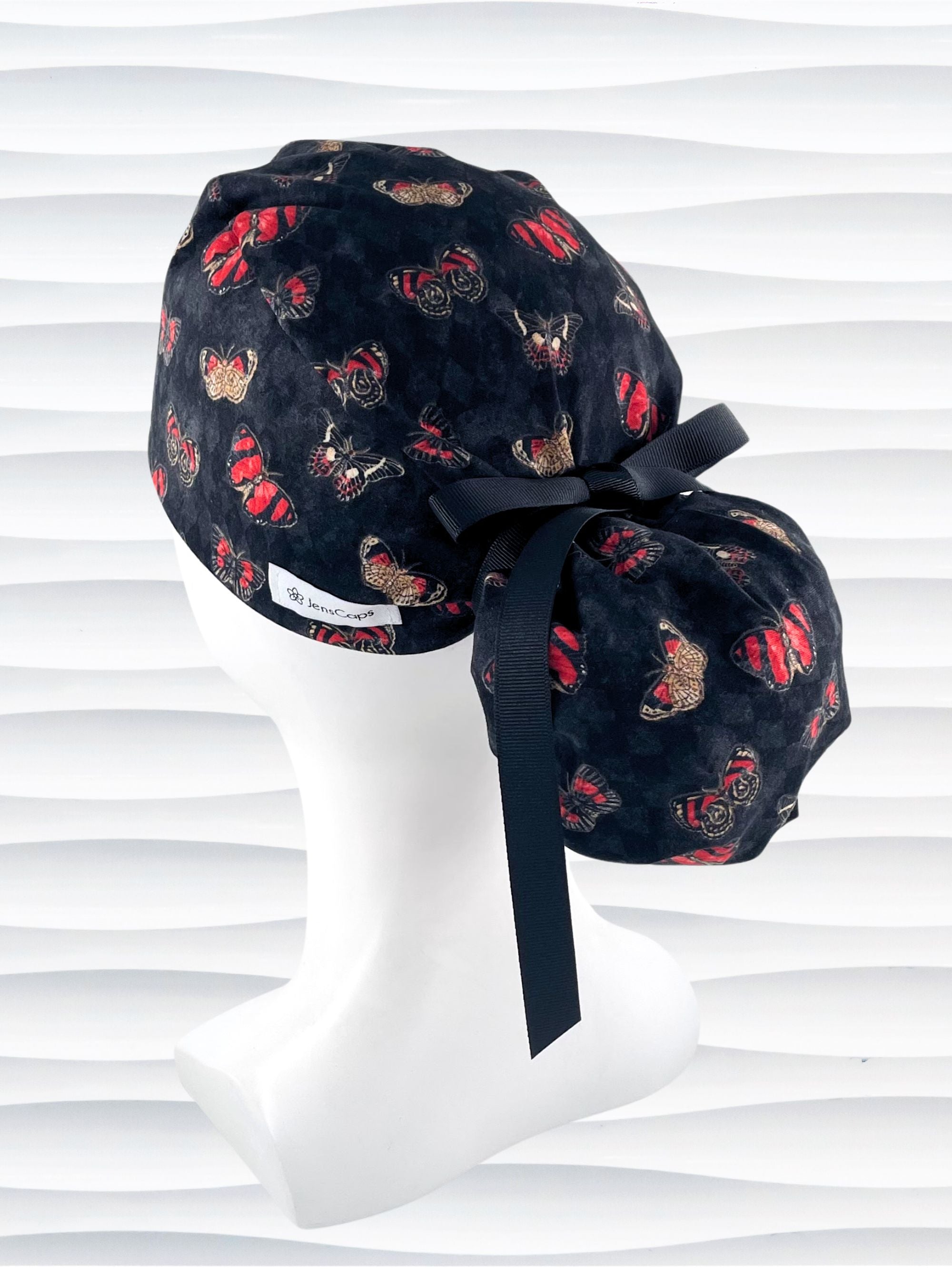 Ponytail style surgical scrub cap hat with red and black butterflies on a black harquin patterned background cotton fabric.