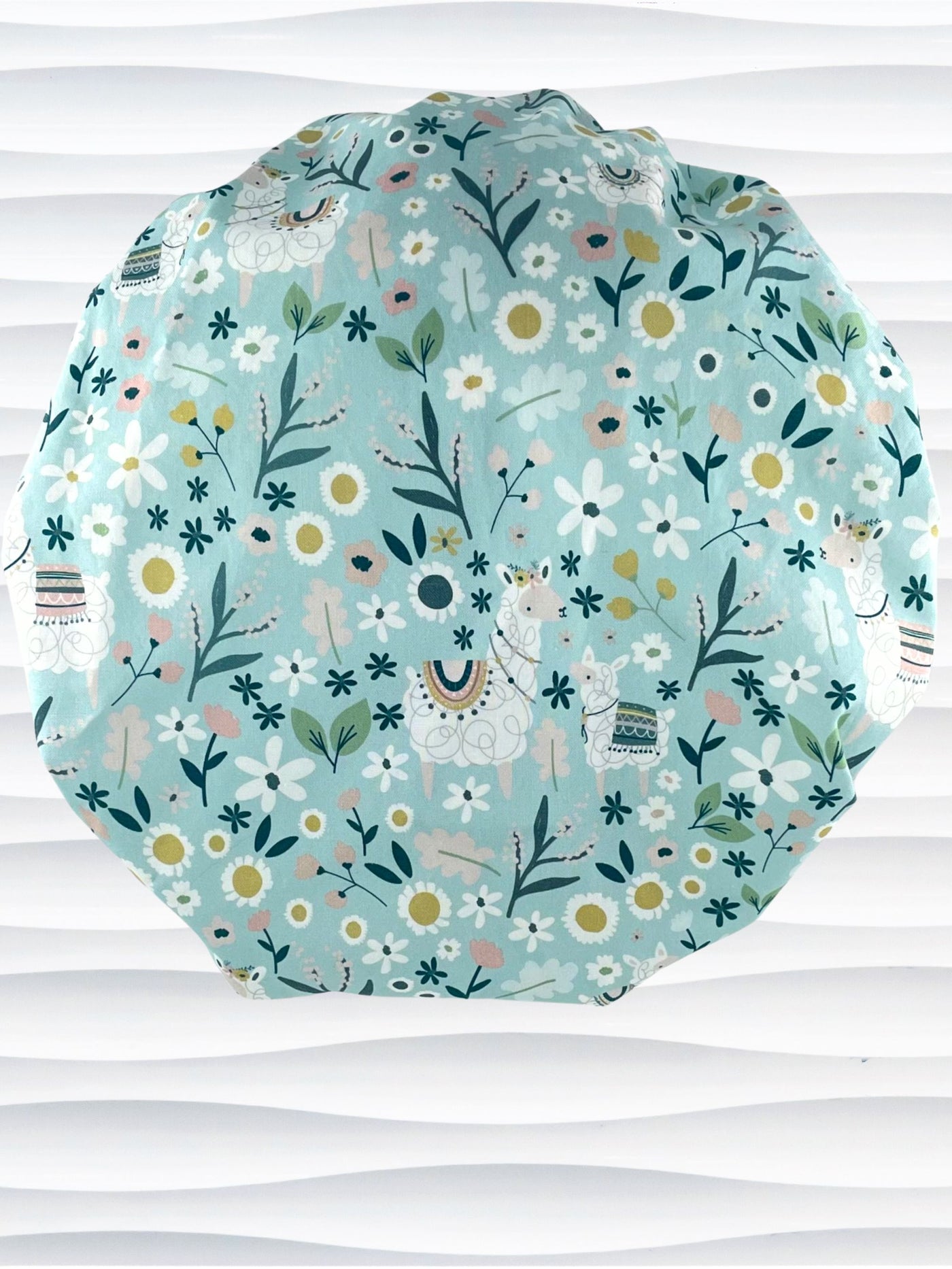 Bouffant style surgical scrub cap hat for long hair with an allover print of llamas, daisies, and flowers in white, pink, and yellow on a light teal cotton fabric.