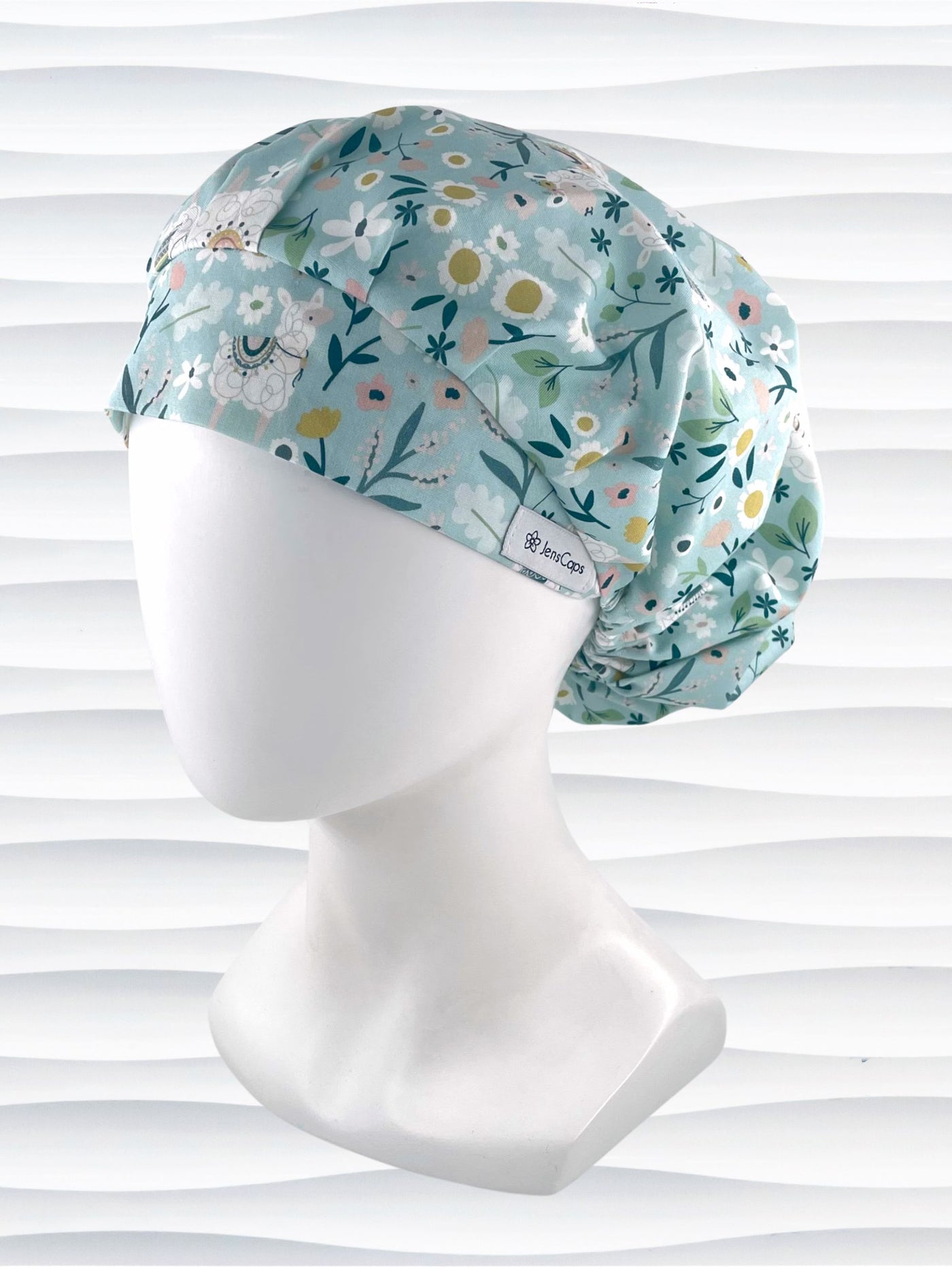 Bouffant style surgical scrub cap hat for long hair with an allover print of llamas, daisies, and flowers in white, pink, and yellow on a light teal cotton fabric.
