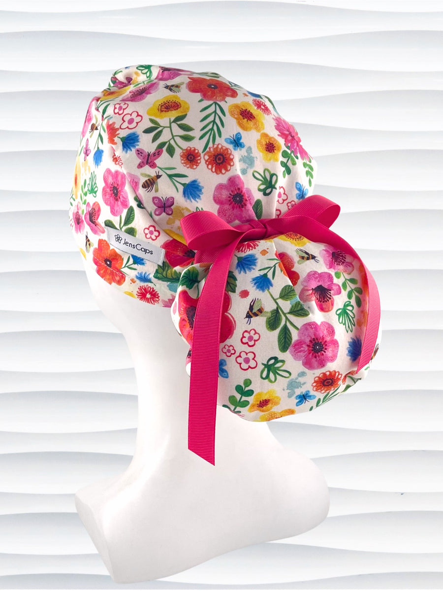 Ponytail style scrub cap hat with flowers and bees and butterflies on white premium cotton and tied with grosgrain ribbon.