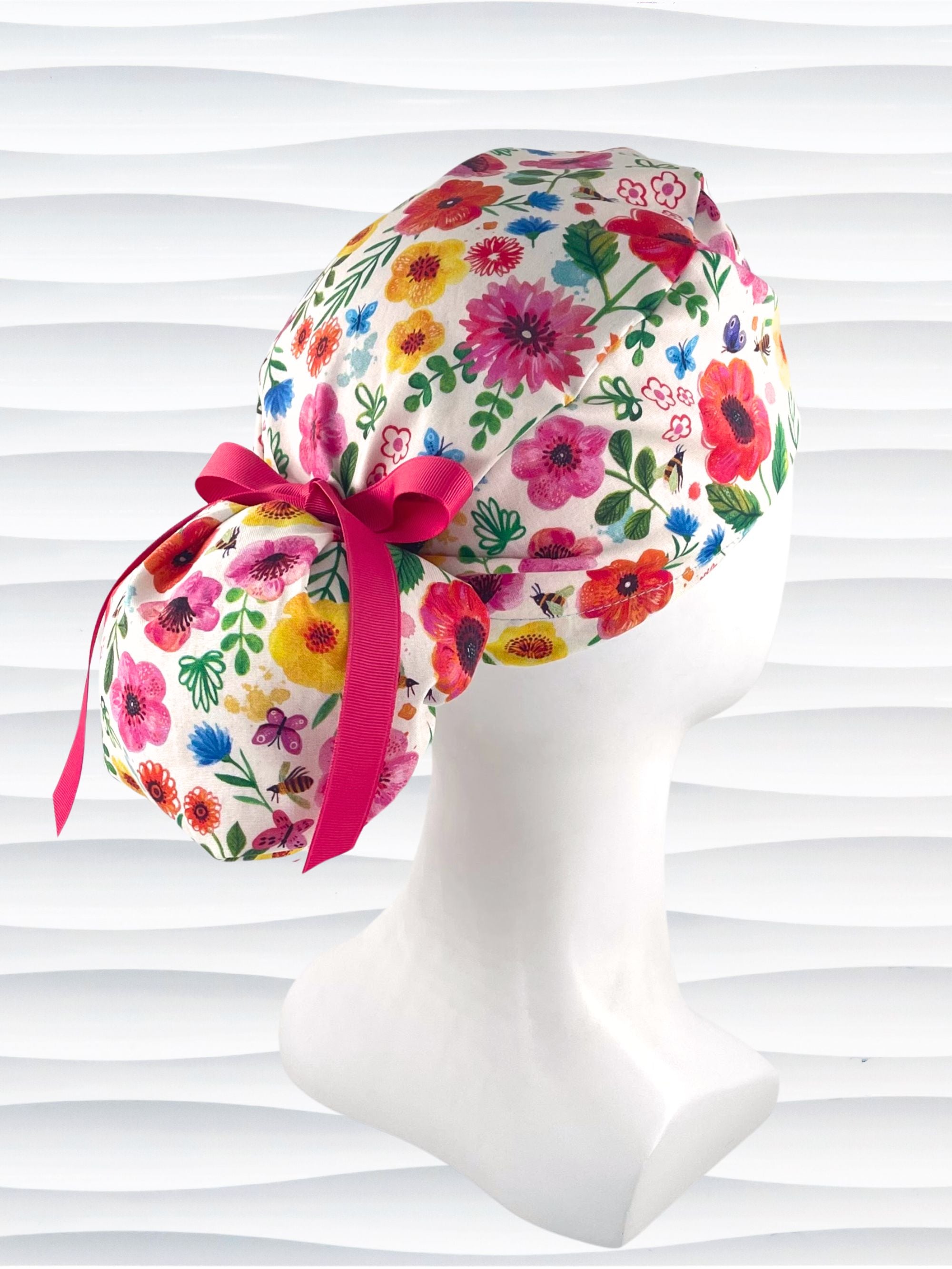 Ponytail style scrub cap hat with flowers and bees and butterflies on white premium cotton and tied with grosgrain ribbon.