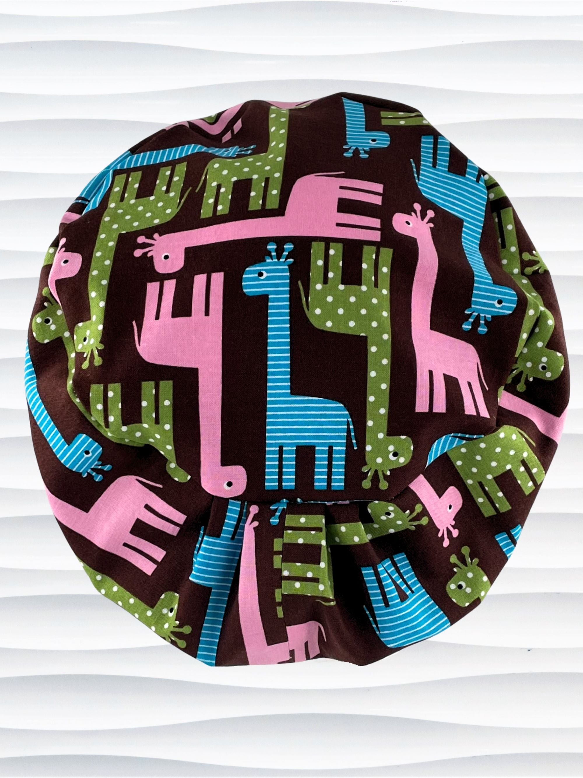 Euro Pixie style surgical scrub cap with cute giraffes with stripes or dots in blue, pink, and green all over a dark brown background on cotton fabric.