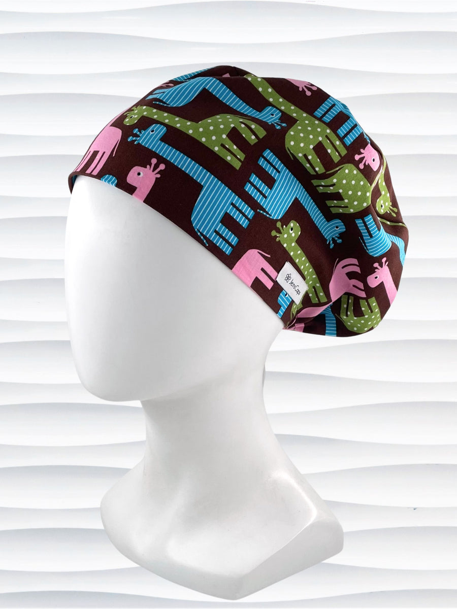 Euro Pixie style surgical scrub cap with cute giraffes with stripes or dots in blue, pink, and green all over a dark brown background on cotton fabric.
