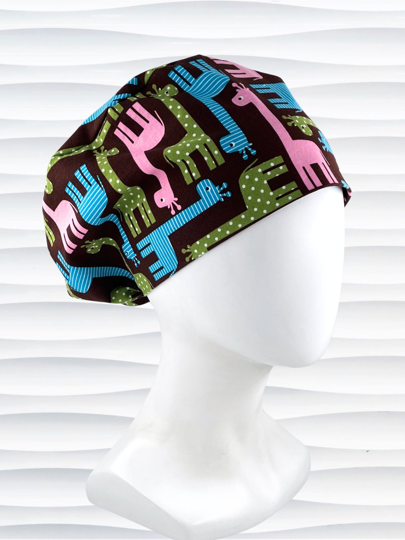 Euro Pixie style surgical scrub cap with cute giraffes with stripes or dots in blue, pink, and green all over a dark brown background on cotton fabric.
