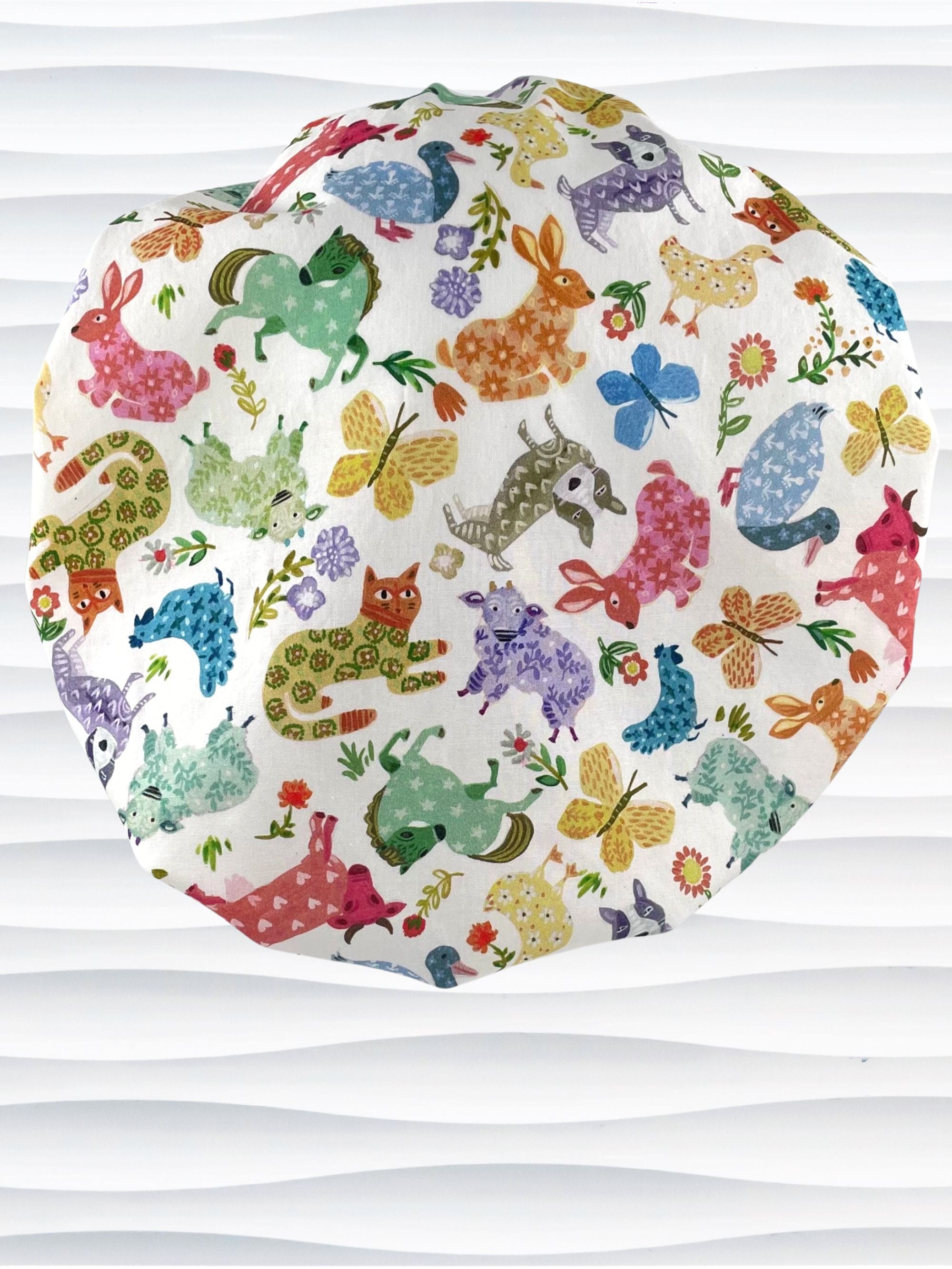 Bouffant style surgical scrub cap with cute and folksy barnyard animals, flowers, and butterflies in red, yellow, green, and blue all over white cotton fabric.