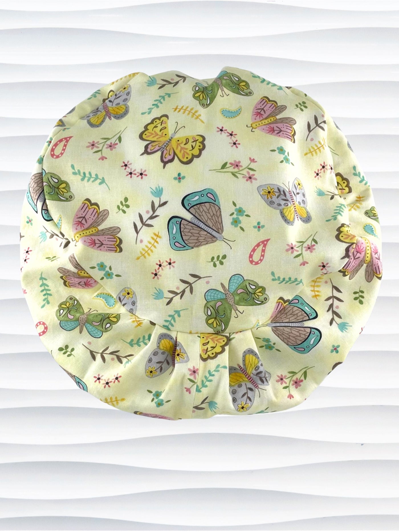 Euro Pixie style surgical scrub cap with butterflies, moths, and flowers in pink, blue, green, and yellow all over a light yellow cotton fabric.
