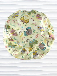 Euro Pixie style surgical scrub cap with butterflies, moths, and flowers in pink, blue, green, and yellow all over a light yellow cotton fabric.