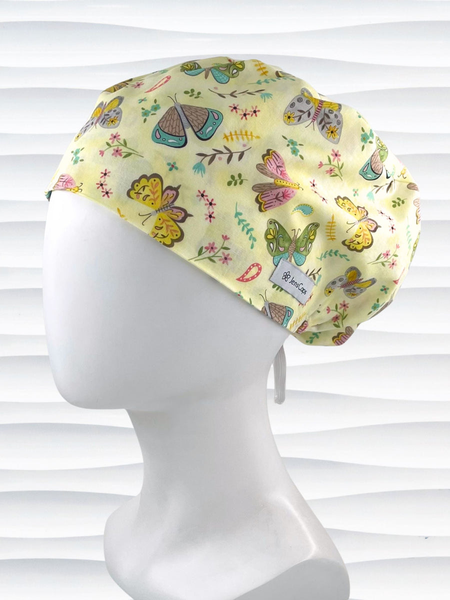 Euro Pixie style surgical scrub cap with butterflies, moths, and flowers in pink, blue, green, and yellow all over a light yellow cotton fabric.
