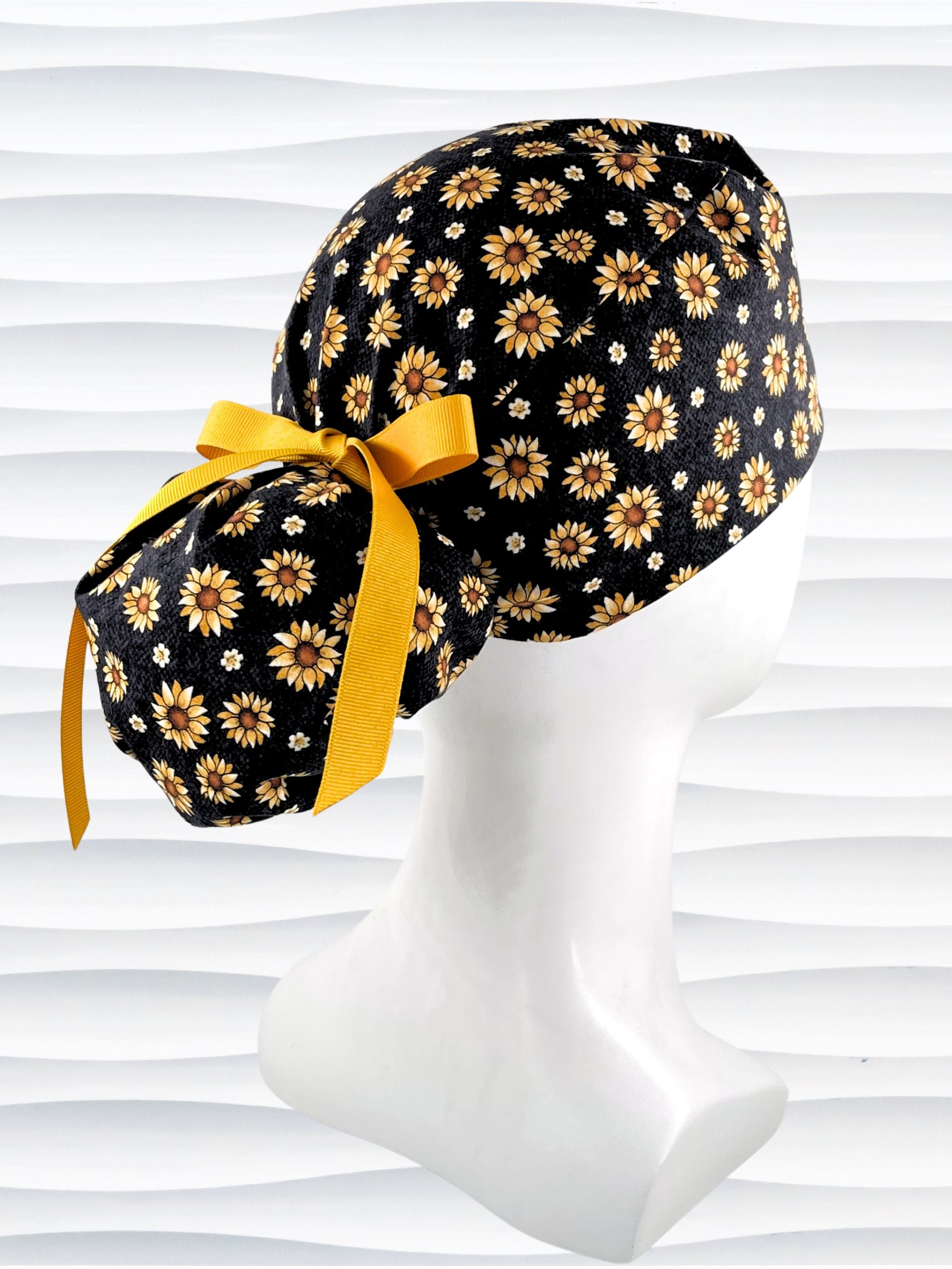 Ponytail style surgical scrub cap hat with sunflowers tossed all over black textured background cotton fabric.