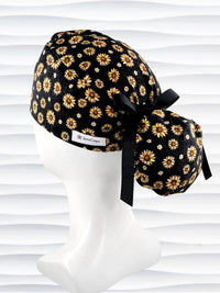 Ponytail style surgical scrub cap hat with sunflowers tossed all over black textured background cotton fabric.