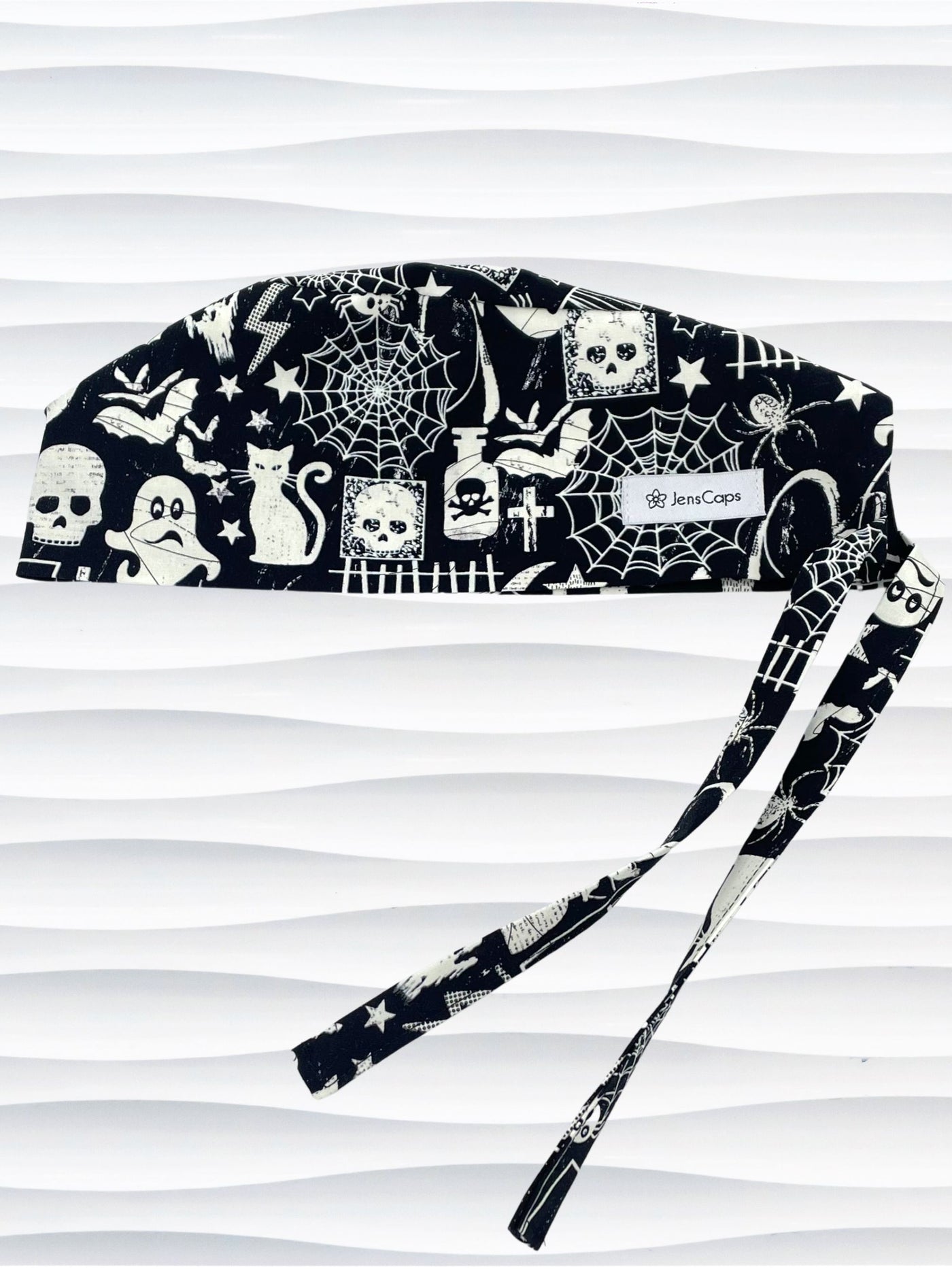 Black and white Halloween-themed Tie back surgical scrub cap with a spiderweb, skull, and ghost pattern, displayed on a white mannequin head
