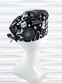 Black and white Halloween-themed Tie back surgical scrub cap with a spiderweb, skull, and ghost pattern, displayed on a white mannequin head