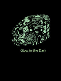 A black graphic featuring a glowing green illustration of a tie back style scrub cap covered in spooky doodles like spiders, skulls, and webs, with the text 'Glow in the Dark' below on a black background.