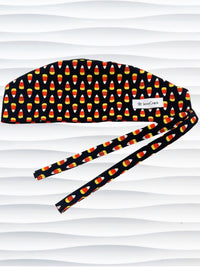 Tie back style surgical scrub cap with with a repeating glow-in-the-dark pattern of orange and yellow candy corn, shown on a black background