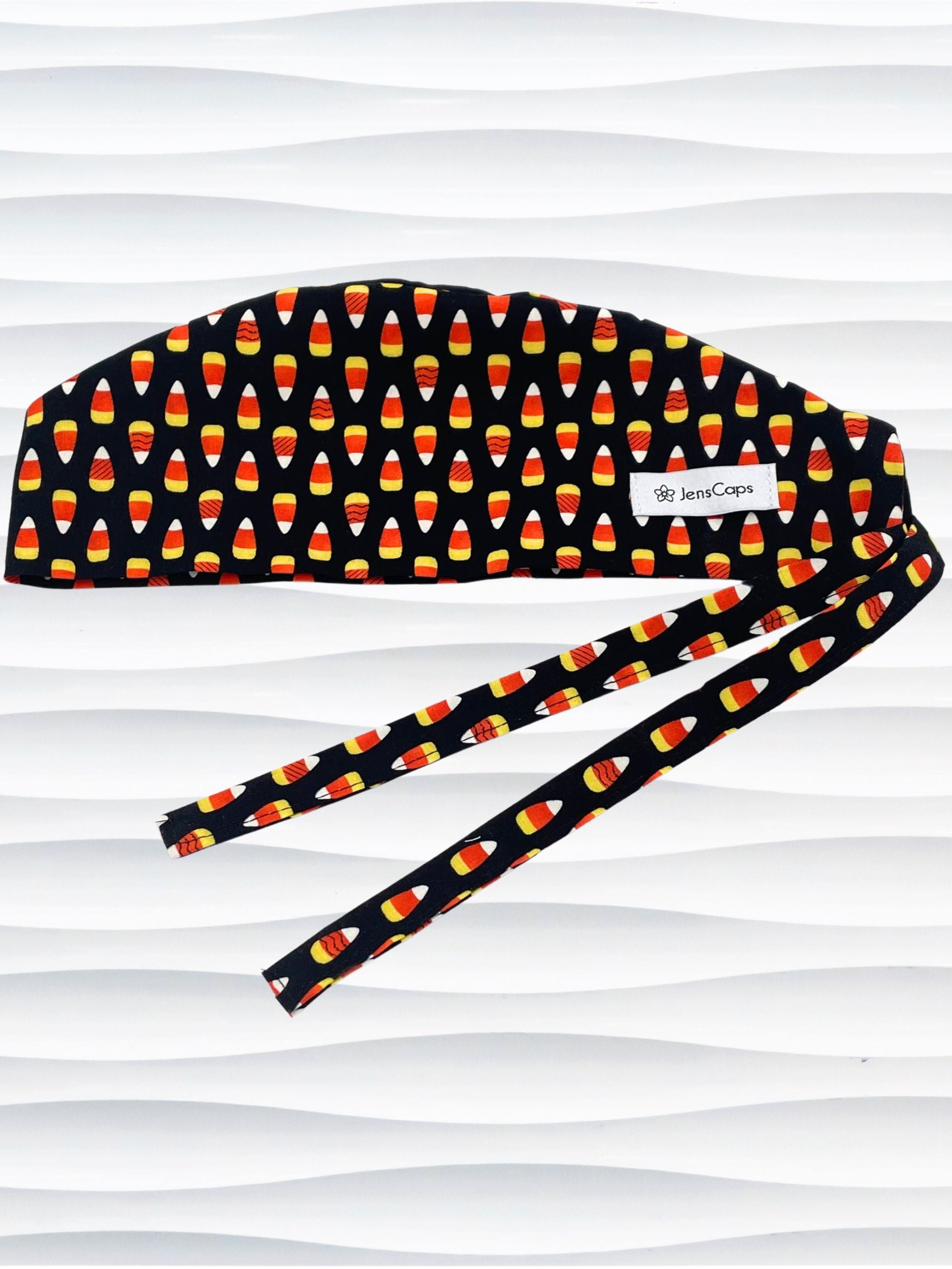 Tie back style surgical scrub cap with with a repeating glow-in-the-dark pattern of orange and yellow candy corn, shown on a black background