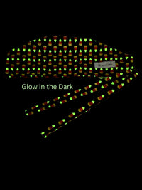 Tie back style surgical scrub cap with with a repeating glow-in-the-dark pattern of orange and yellow candy corn, shown on a black background with the text 'Glow in the Dark'
