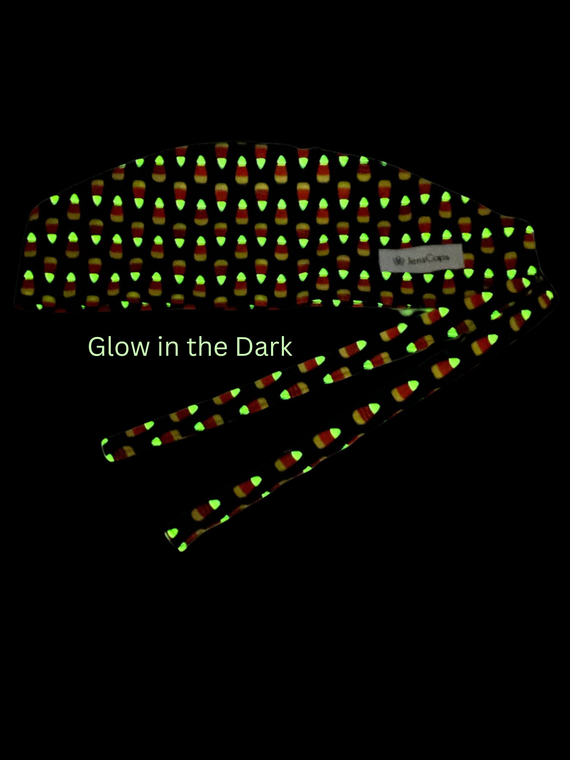 Tie back style surgical scrub cap with with a repeating glow-in-the-dark pattern of orange and yellow candy corn, shown on a black background with the text 'Glow in the Dark'
