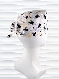 A tie-back style surgical scrub cap by JensCaps with a black cat silhouette pattern and subtle purple and gold speckles, displayed on a white mannequin head against a wavy white background